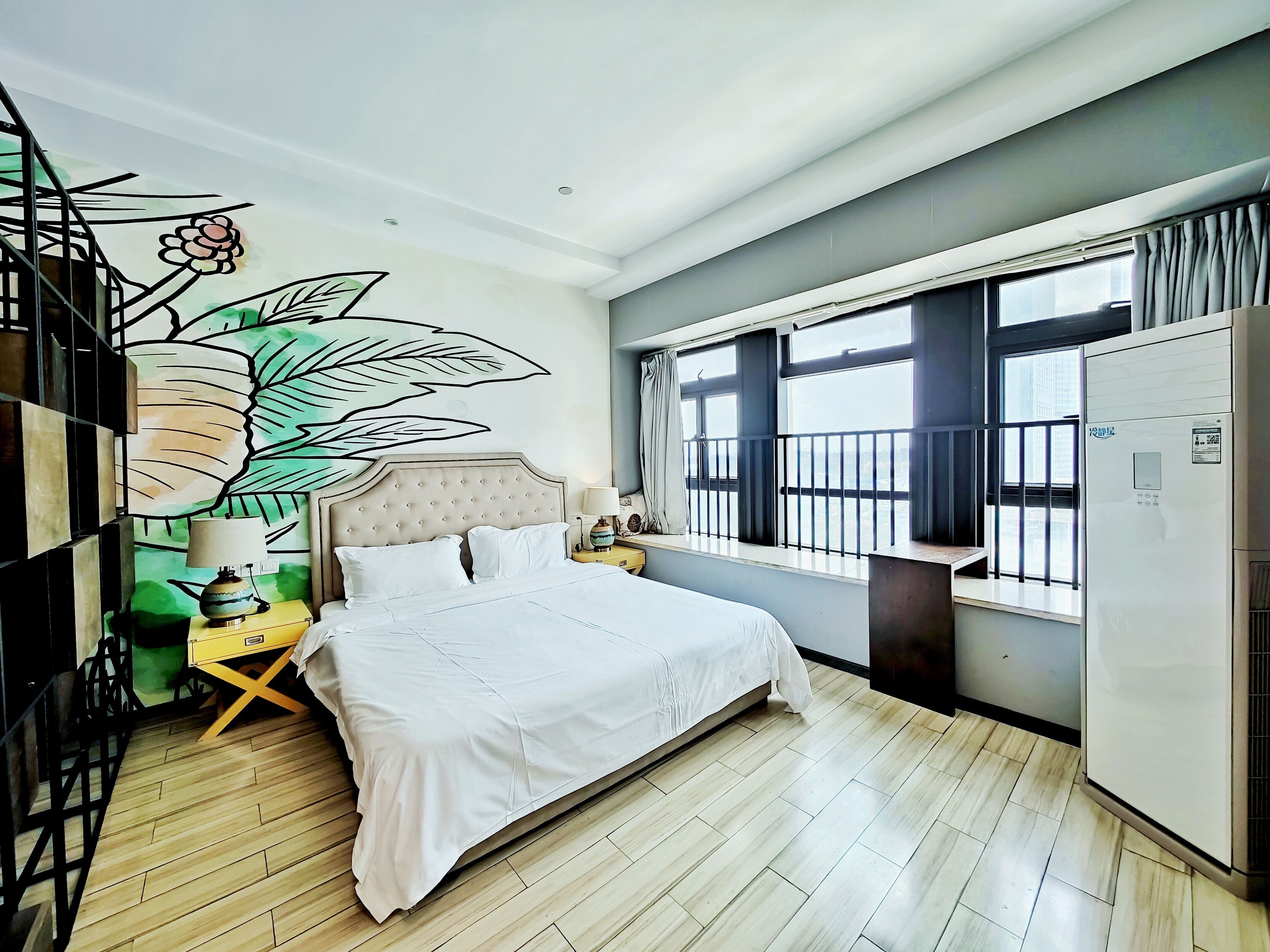 Une chambre à coucher avec un lit, une fenêtre donnant sur un beau paysage, un radiateur et un mur décoré de motifs de feuilles.