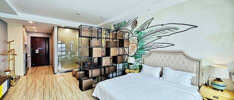 A hotel room with a large bed, a wooden floor, a decorative wall panel, and a view into the hallway.
