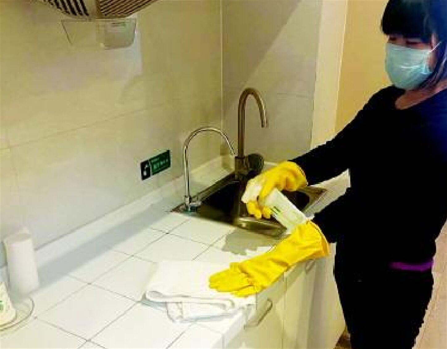 Eine Person reinigt ein Waschbecken im Badezimmer mit einem Handtuch und einem Reinigungstuch.