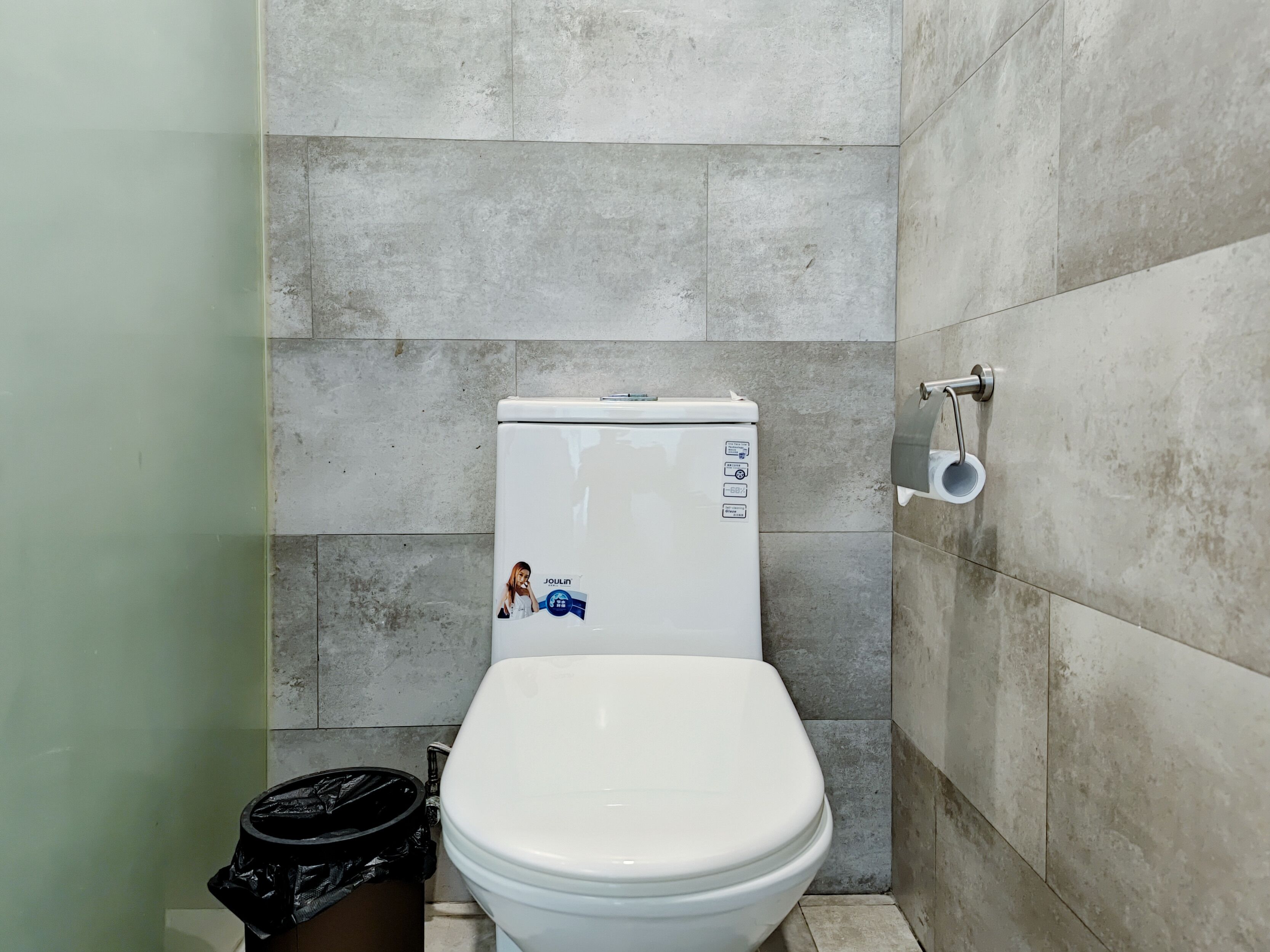 A bathroom with a white toilet, a black trash bin, and a toilet paper holder on the wall.