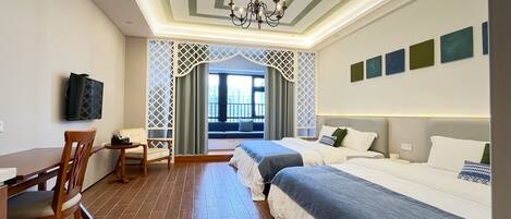 A hotel room with a wooden dining table, two beds, a TV mounted on the wall, and a view of the city through a window with a lattice design.