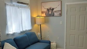 Una sala de estar con un sofá azul, una lámpara, aire acondicionado y una puerta.