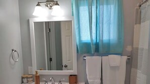 Un baño con tocador blanco, espejo, lavamanos y zona de ducha con cortina.