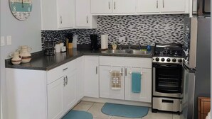 Una cocina compacta con armarios blancos, una encimera negra, una estufa y un microondas. Hay dos felpudos azules en el suelo.