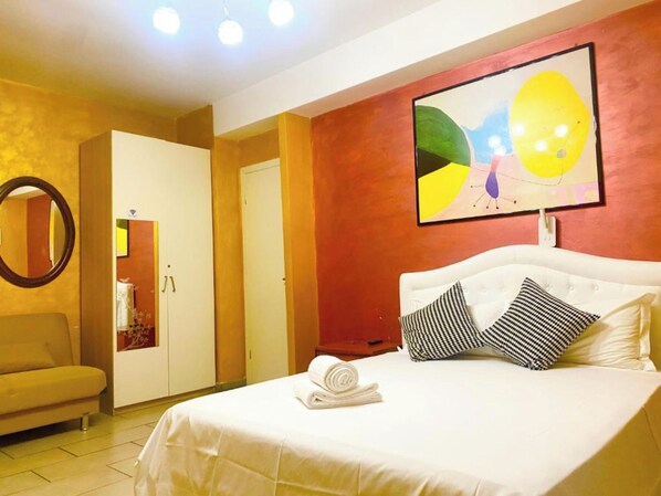 Quarto de hotel com cama, sofá, espelho e um quadro na parede.