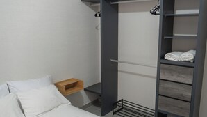 Een slaapkamer met een bed, een houten nachtkastje, een inbouw-kledingkast met planken, en een hangende schoenenrek.