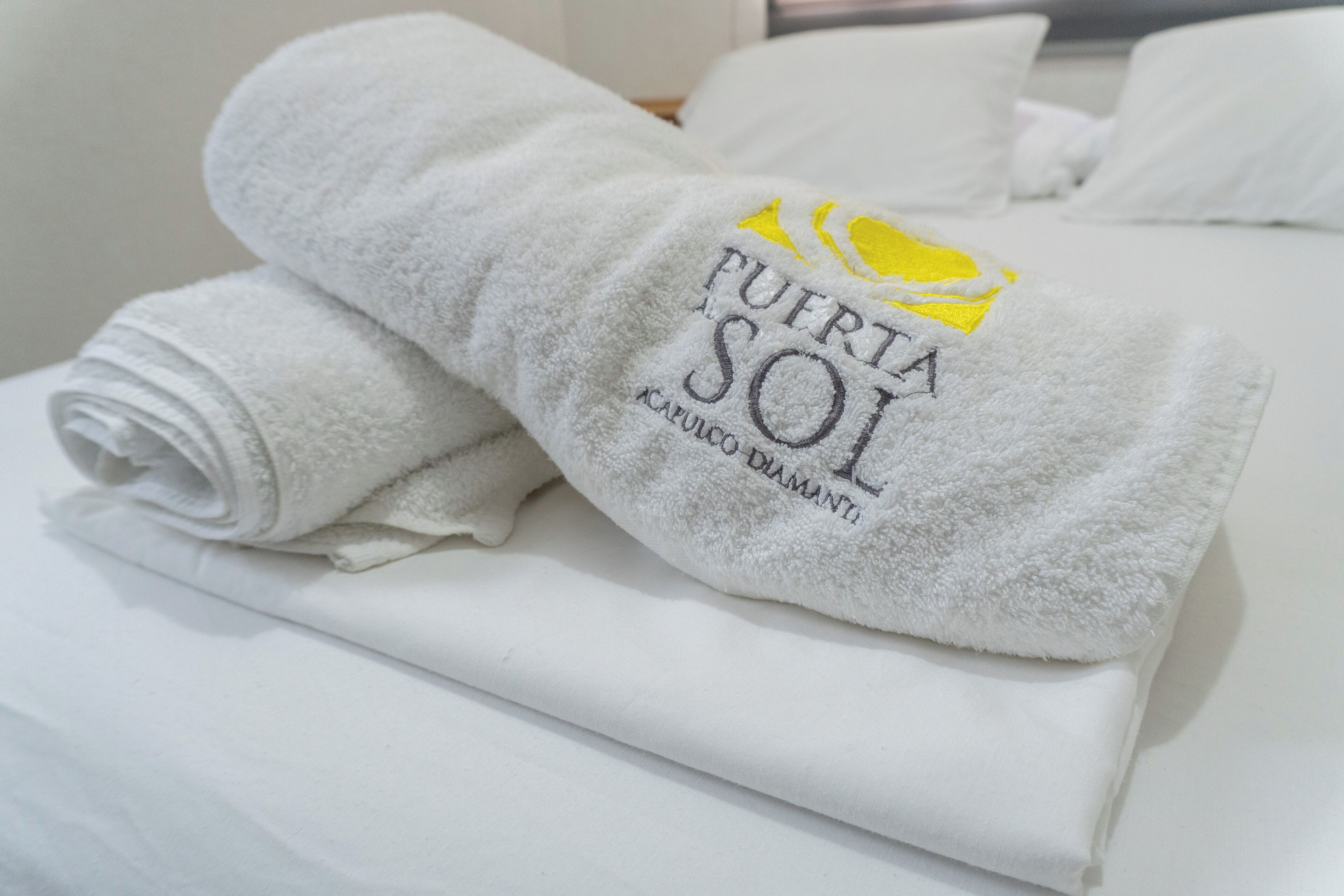 Uma toalha branca e dobrada com texto bordado e um logo amarelo sobre a cama.