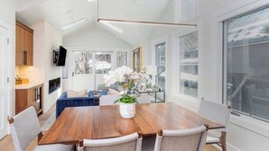 A modern dining area with a wooden table, grey upholstered chairs, and a potted orchid centerpiece.