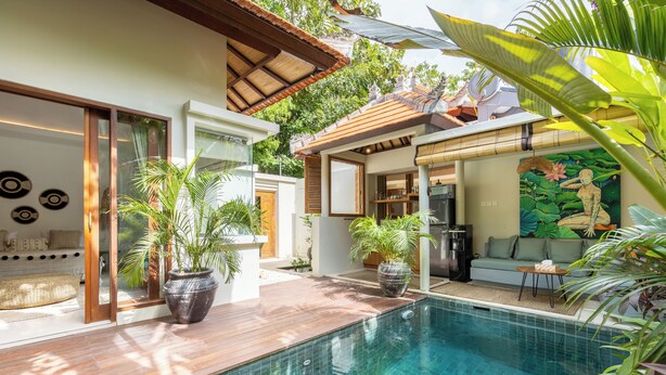 A modern pool area with a wooden deck, potted plants, and a dining area with a mural. - Villa Jamu Bingin (Pecatu)