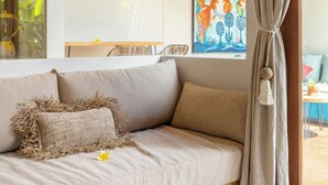 A modern living room with a beige sofa, a wooden coffee table, and a large window with a view of greenery. - Villa Jamu Bingin (Pecatu)