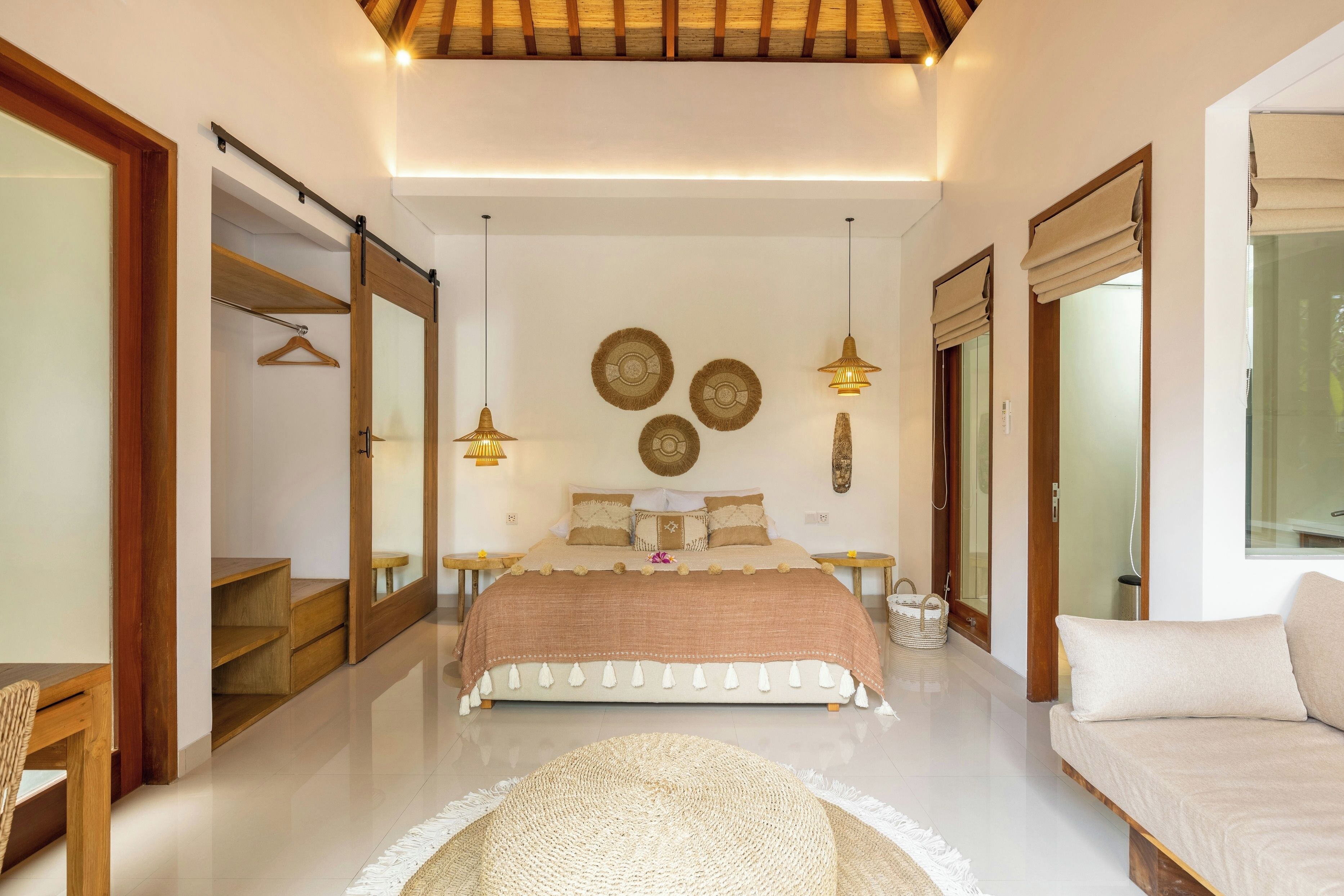 A modern bedroom with a large bed, bedside tables, a sofa, and a mirror.