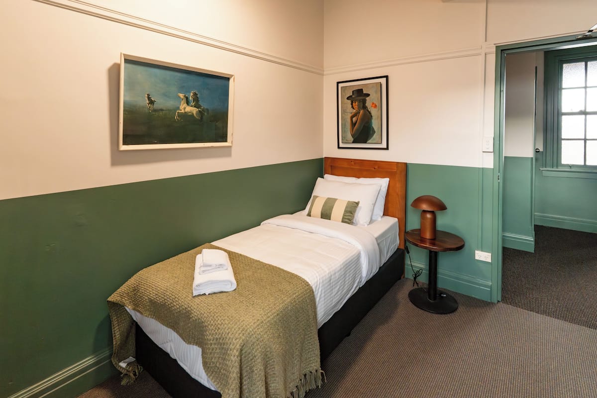 Cama bem arrumada com parede listrada em verde e branco, uma pintura de cavalos e um retrato de mulher.