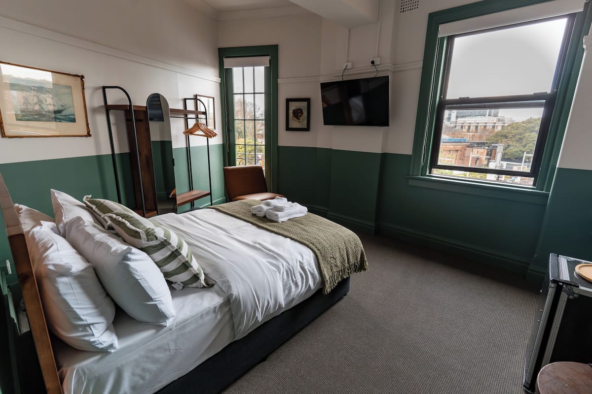 Quarto bem arrumado com cama, cadeira, janela com vista e televisão na parede.