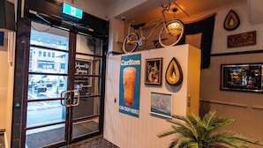 Entrada de un hotel con puerta de vidrio, una bicicleta colgada en la pared, un cartel de Carlton y una fotografía enmarcada de un perro.