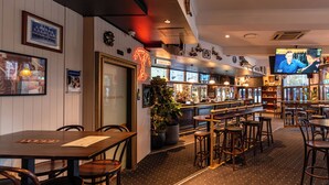 Zona de bar con mesas y taburetes de madera, un letrero de neón y una pantalla de televisión.