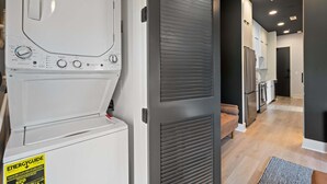 Un cuarto de lavado con lavadora y secadora de carga frontal, un banco y una puerta con picaporte de metal.