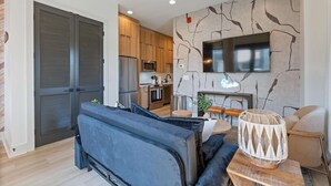 A modern living room with a sofa, a coffee table, and a TV. - Kay’s Perch • Modern 1BR Corner Retreat (Nashville)