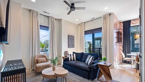 A modern living room with a dark sofa, a round wooden table, a chair, and a ceiling fan. - Kay’s Perch • Modern 1BR Corner Retreat (Nashville)
