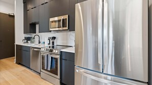 A modern kitchen with stainless steel appliances, dark cabinetry, and a white countertop.