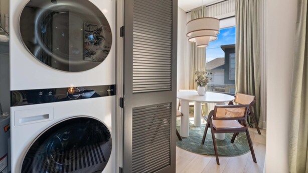 A modern hotel room with a washing machine, a dining area with a table and chairs, and a view of the outside.