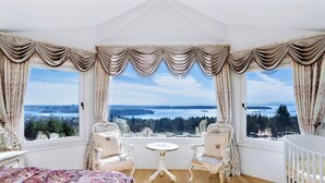 A room with a bed, two chairs, a crib, and a view of a lake and city.