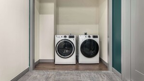 A laundry room with two front-loading washing machines and a grey carpeted floor. - Cozy Stay Next To Atrium Hospital | Walk Score 74; Mercer Music at Capricorn – ~12-minute walk (0.6 miles) (Macon)