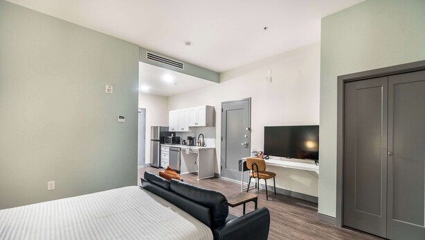 A modern hotel room with a bed, a desk, a chair, and a kitchenette. - Right Next To Atrium Hospital | ADA-Friendly Stay (Macon)