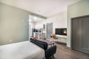 A modern hotel room with a bed, a desk, a chair, a kitchenette, and a TV. - Right Next To Atrium Hospital | ADA-Friendly Stay (Macon)