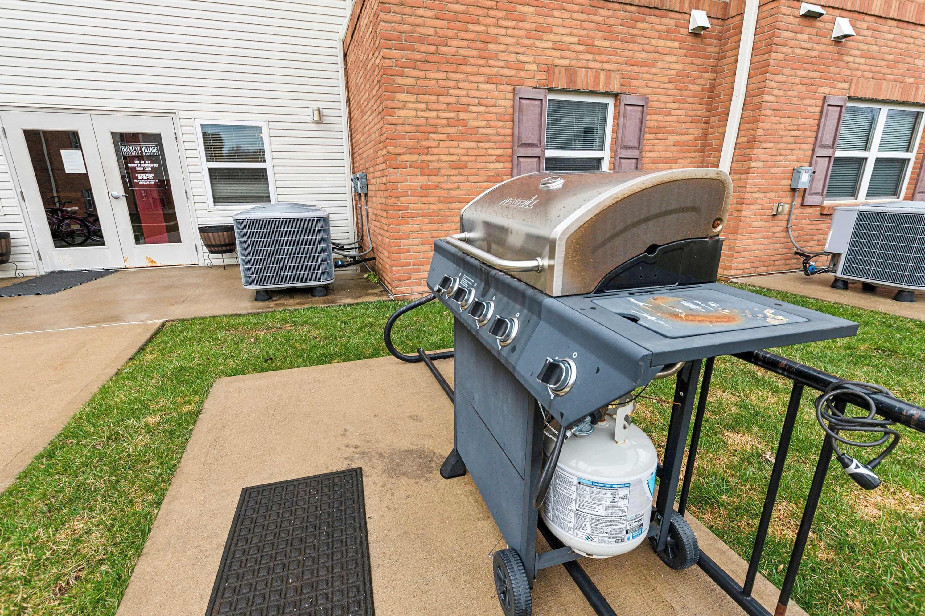 An outdoor grill setup with a propane tank, positioned in front of a brick building with a door and windows.