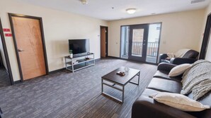 A modern living room with a dark wood floor, a flat-screen TV on a stand, a sofa with a blanket, and a door marked with 'A' and 'B'.