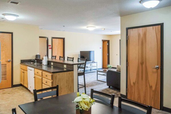 A modern hotel room with a kitchen area, a dining table with chairs, and a sofa in the living area.