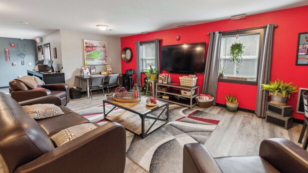 A modern living room with a red accent wall, leather sofas, a wooden coffee table, and a flat-screen TV. - Modern Retreat Near Campus & Local Trails (Mansfield)