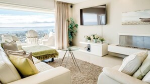 A modern living room with a city view, a flat-screen TV, a fireplace, and a comfortable seating area. - Spacious 3Bed Apt Overlooking Cape Town Panova (Cape Town)