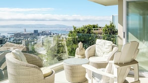 A balcony with wicker furniture, a glass table, and a view of a cityscape and water. - Spacious 3Bed Apt Overlooking Cape Town Panova (Cape Town)