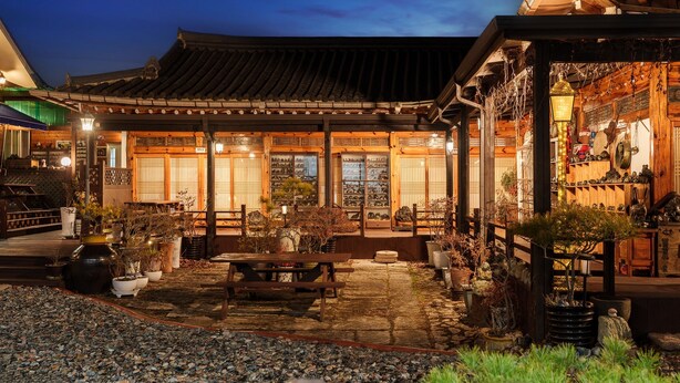 A traditional Japanese building with a tiled roof, wooden structures, and a garden area with potted plants and a stone pathway. - Gyeongju Silla Palace Pension (Gyeongju)