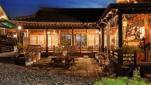 Ein traditionelles japanisches Gebäude mit einem Ziegeldach, Holzkonstruktionen und einem Garten mit Blumentöpfen und einem Kiesweg.