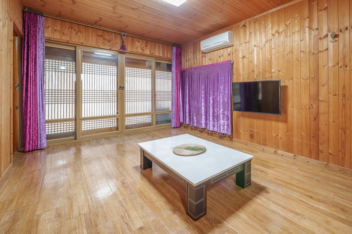 Ein Zimmer mit Holzwänden, einer Schiebeglasdoor, einem Flachbildfernseher und einem kleinen Tisch mit einer gewebten Unterlage.