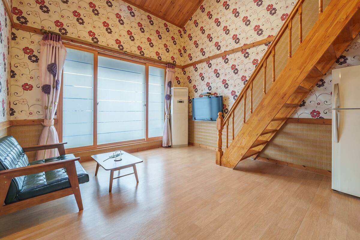 Ein gemütliches Wohnzimmer mit einer Holztreppe, einer Couch, einem kleinen Tisch und einem Kühlschrank.