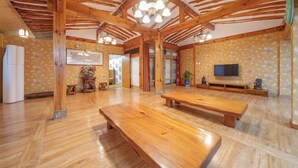 A spacious room with wooden flooring, a large wooden bench, a television, and a decorative wall with a floral pattern. - Gyeongju Silla Palace Pension (Gyeongju)