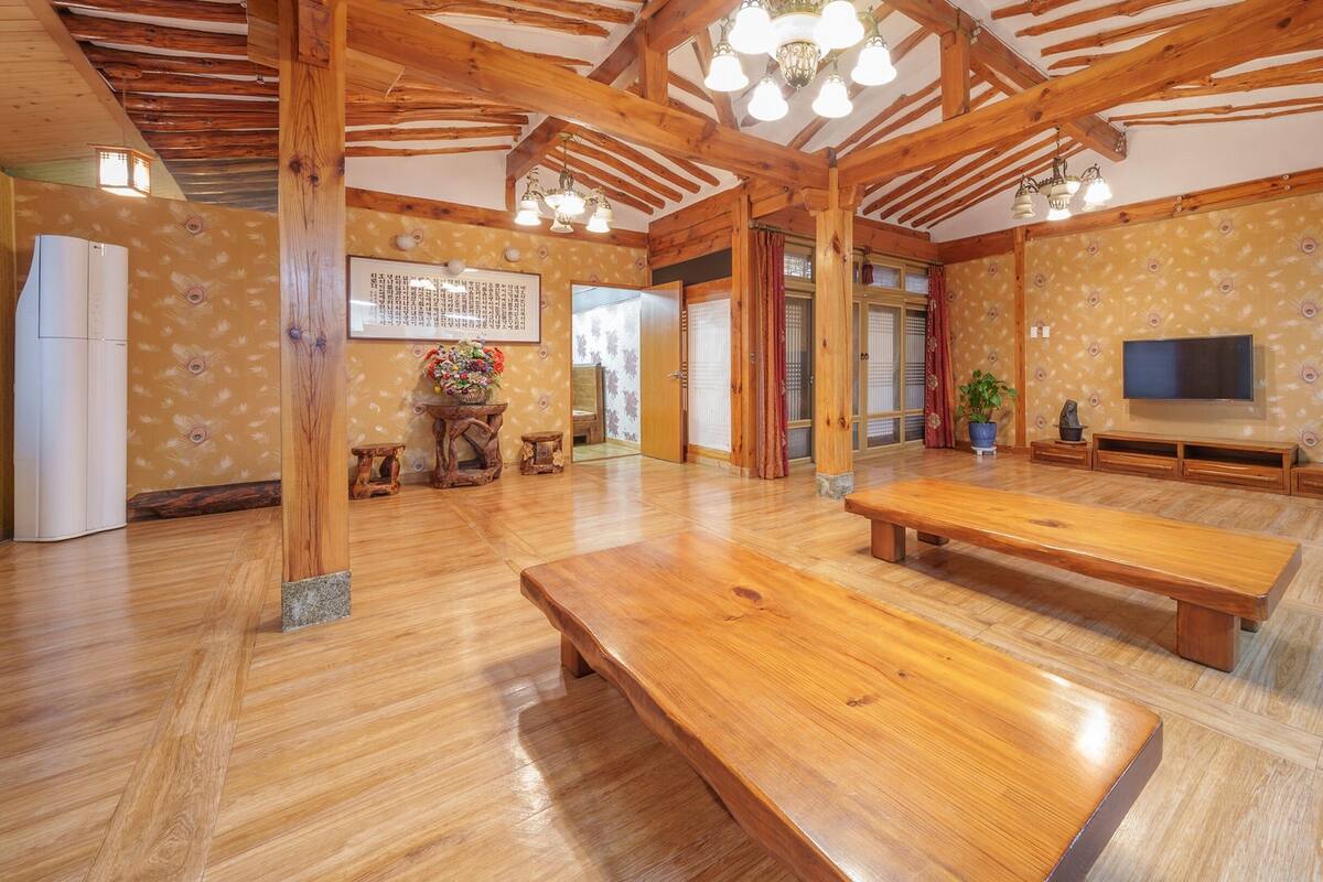 Ein geräumiger Raum mit Holzboden, einer großen Holzbank, einem Fernseher und einer Wand mit floralem Dekor.