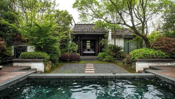 Edificio tradicional japonés con tejado de baldosas, rodeado de exuberante vegetación y un estanque de carpas en primer plano.