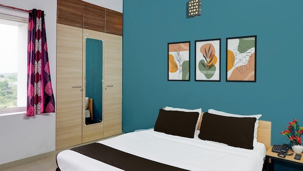 Een slaapkamer met een bed, een garderobe, een nachtkastje met telefoon en vaas, en drie kunstwerken met bladmotieven aan de muur.