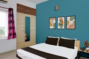 Une chambre à coucher comprenant un lit, une armoire, une table de chevet avec un téléphone et un vase, et trois œuvres d’art représentant des feuilles, encadrées et accrochées au mur.