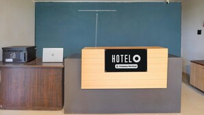 Een receptiebalie met een bordje waarop 'HOTELO Company-Serviced' staat en een laptop op het aanrecht.