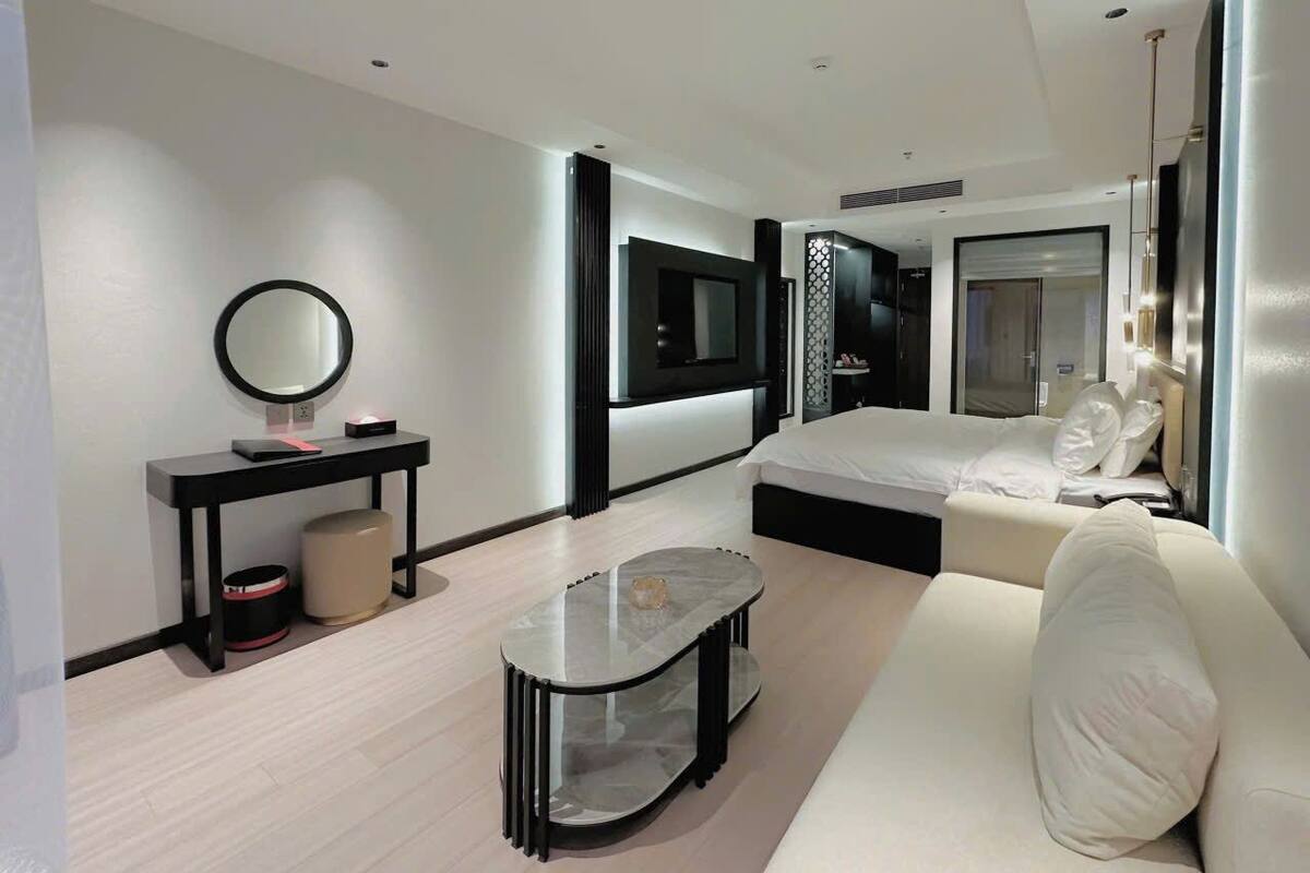 A modern hotel room with a bed, a sofa, a small table, a mirror, and a TV.