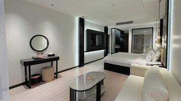 A modern hotel room with a bed, a sofa, a small table, a mirror, and a TV.