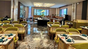 A hotel dining area with multiple tables, chairs, and a central kitchen area. - GARDEN PHOENIX HOTEL (Vu Ninh)