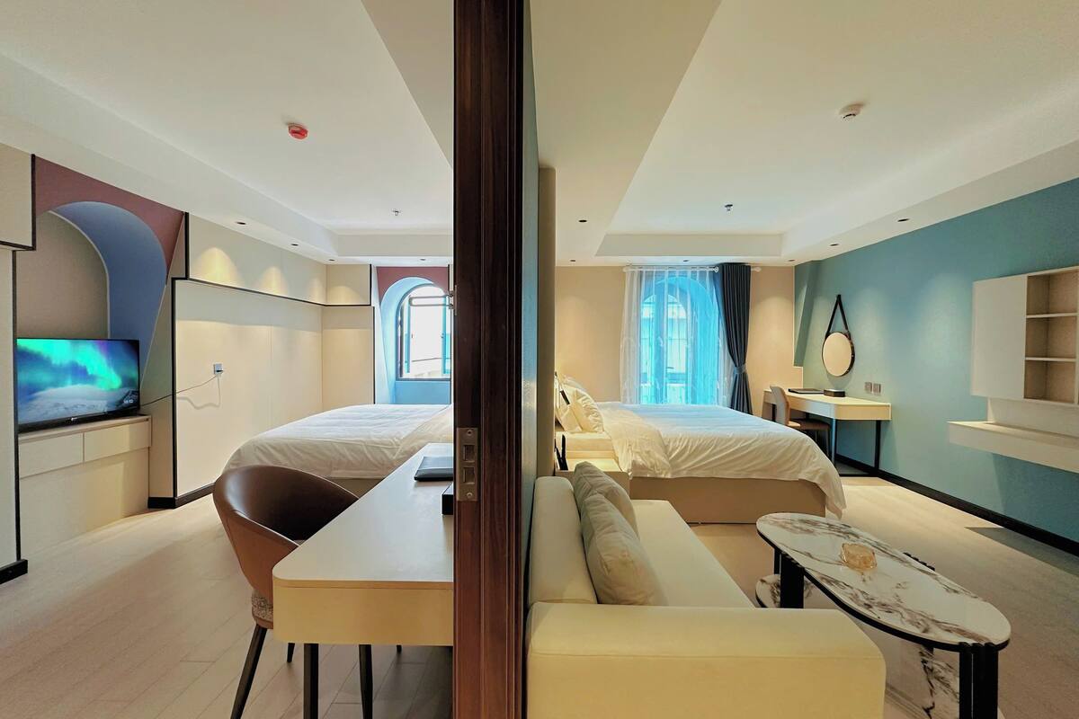 A modern hotel room with a bed, a desk, a chair, a TV, and a bathroom.