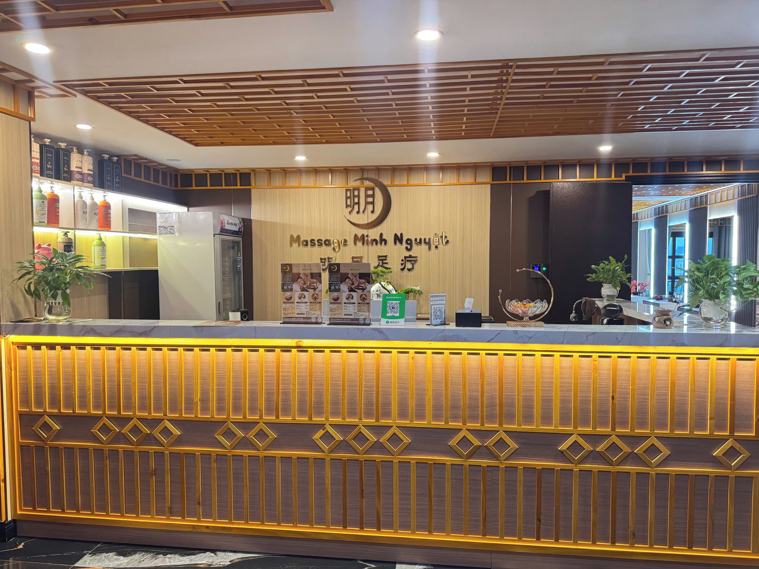 A reception desk with a wooden panel design, a wall-mounted sign for a massage clinic, and a counter with various items including a plant and a small bowl.