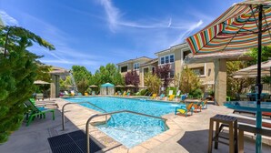 Une piscine entourée de bâtiments et de verdure, avec des chaises longues et des parasols.